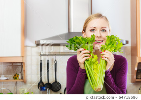 Woman in kitchen holds green celery Woman in kitchen holds green celery 64718686