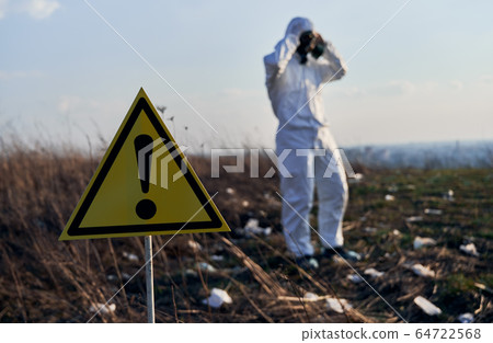 Ecologist walking in garbage dump field with warning sign. 64722568