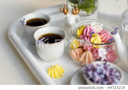Breakfast with black tea or coffee and sweet meringue kisses on the white table. Breakfast with black tea or coffee and sweet meringue kisses on the white table. 64725219