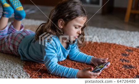 Cute little girl lying down looking at mobile 64726480