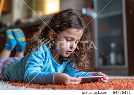 Cute little girl lying down looking at mobile 64726481