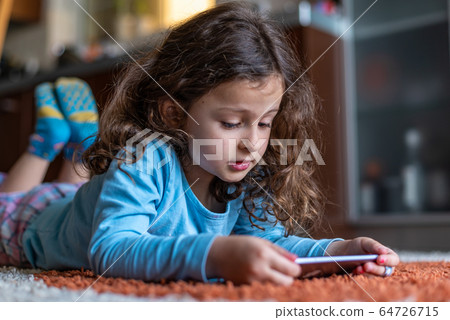 Cute little girl lying down looking at mobile 64726715