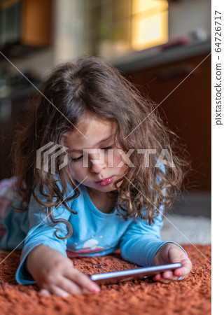 Cute little girl lying down looking at mobile 64726717