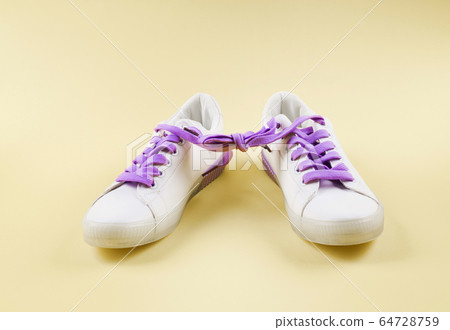White sneakers with tied purple laces on beige White sneakers with tied purple laces on beige 64728759