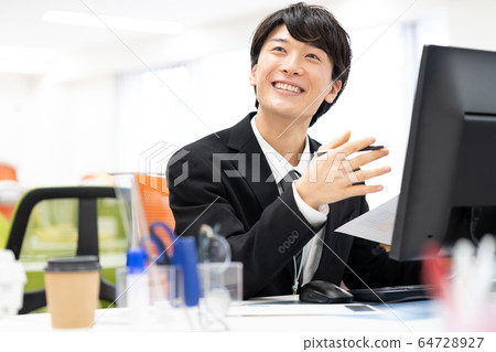 Smiling young male employee in office Smiling young male employee in office 64728927