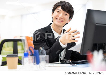 微笑的年輕男性僱員在辦公室 微笑的年輕男性僱員在辦公室 64728928