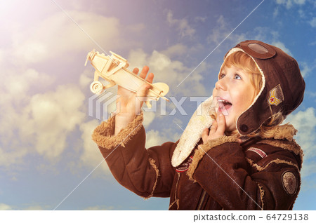 Cute little boy aviator wit wooden plane toy against blue sky background 64729138