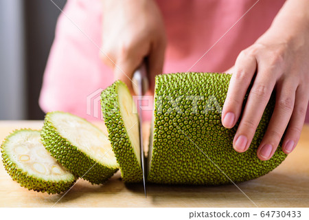 Hand holding kitchen knife and cutting young jackfruit on wooden board for cooking, Asian food 64730433