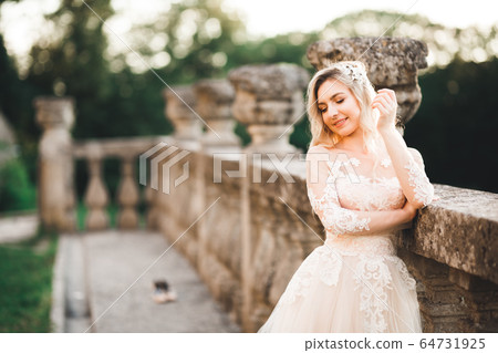 Beautiful brunette bride in elegant white dress holding bouquet posing near castle 64731925