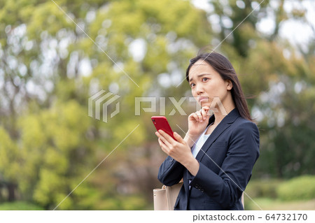 Worried young woman looking at smartphone outdoors 64732170