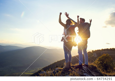 happy couple man and woman tourist at top of mountain at sunset outdoors during a hike in summer 64734291
