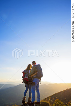 Hikers with backpacks relaxing on top of a mountain and enjoying the view of valley 64734756
