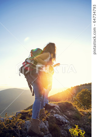 Hikers with backpacks relaxing on top of a mountain and enjoying the view of valley 64734793
