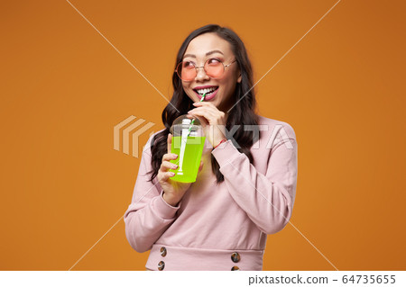 Happy woman in pink glasses with cocktail on empty yellow background 64735655