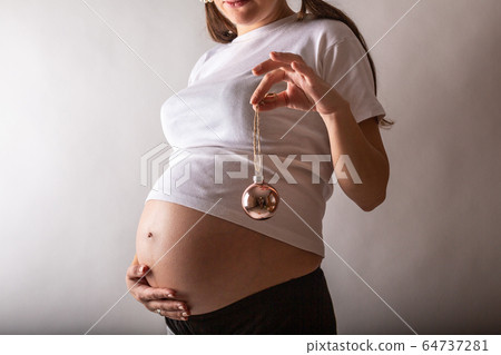 Pregnant woman smiling, touching her belly, standing over white wall. Copy space. Christmas, New year concept. 64737281