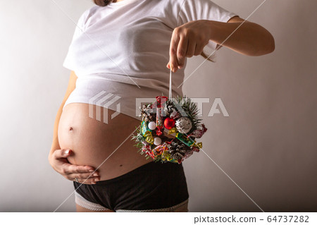 Pregnant woman smiling, touching her belly, standing over white wall. Copy space. Christmas, New year concept. Pregnant woman smiling, touching her belly, standing over white wall. Copy space. Christmas, New year concept. 64737282