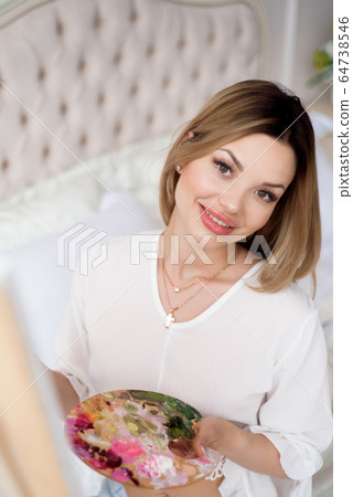 Young beautiful woman artist painting at home pink peonies 64738546