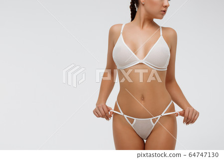 Woman in white lingerie holding laces of underwear Woman in white lingerie holding laces of underwear 64747130