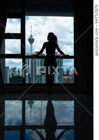 A slender girl is looking at the city through a 64752970