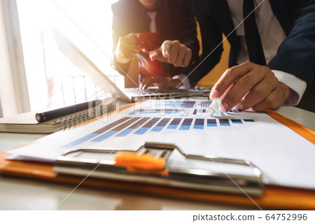 Business documents on office table with smart phone and laptop and two colleagues discussing data in the background in morning light Business documents on office table with smart phone and laptop and two colleagues discussing data in the background in morning light 64752996