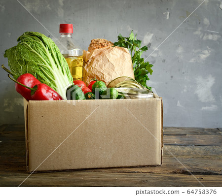 Food in a cardboard box. Food donation or food delivery concept. Light background. Free space for text. Oil, cabbage, salad, vegetables, canned food. 64758376