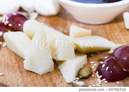 Several types of cheese on a wooden plate with berry sauce. Several types of cheese on a wooden plate with berry sauce. 64760336