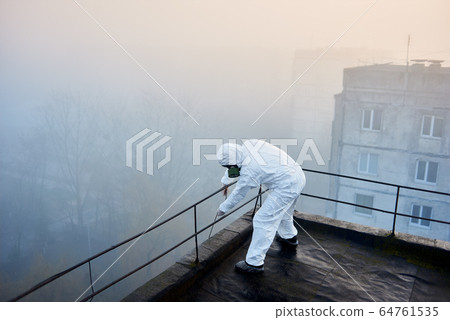 Worker scientist wearing protective coverall and gas mask doing ecological tests on the roof 64761535