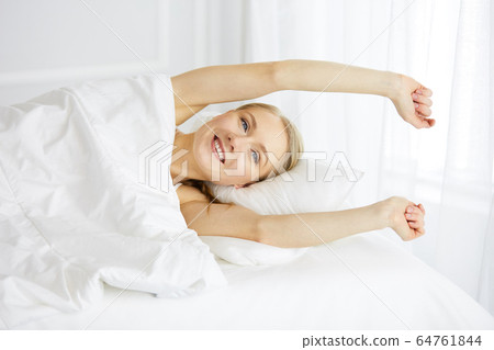 Smiling woman stretching hands in bed after waking up, entering a day happy and relaxed after good night sleep. Sweet dreams, fairy morning concept 64761844