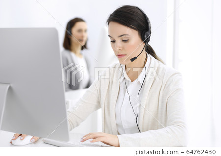 Call center. Casual dressed woman sitting in headset at customer service office. Group of operators at work. Business concept 64762430