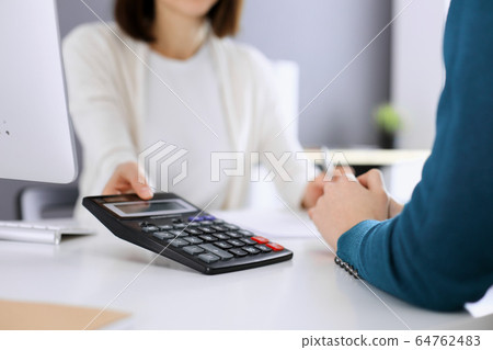 Accountant checking financial statement or counting by calculator income for tax form, hands closeup. Business woman sitting and working with colleague at the desk in office toned in blue. Tax and Accountant checking financial statement or counting by calculator income for tax form, hands closeup. Business woman sitting and working with colleague at the desk in office toned in blue. Tax and 64762483