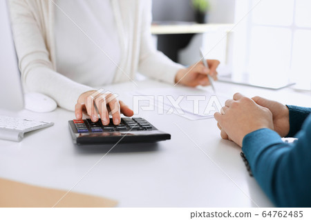 Accountant checking financial statement or counting by calculator income for tax form, hands closeup. Business woman sitting and working with colleague at the desk in office toned in blue. Tax and Accountant checking financial statement or counting by calculator income for tax form, hands closeup. Business woman sitting and working with colleague at the desk in office toned in blue. Tax and 64762485