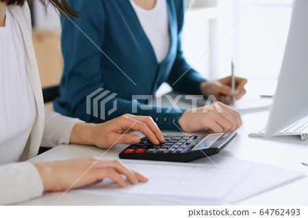 Accountant checking financial statement or counting by calculator income for tax form, hands closeup. Business woman sitting and working with colleague at the desk in office toned in blue. Tax and Accountant checking financial statement or counting by calculator income for tax form, hands closeup. Business woman sitting and working with colleague at the desk in office toned in blue. Tax and 64762493