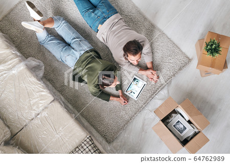 Overview of young contemporary couple in casualwear lying on unrolled rug 64762989