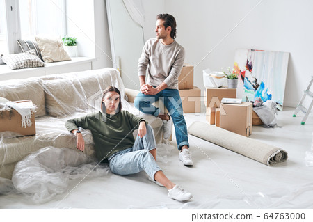 Young female sitting on the floor while her husband on couch staring in window 64763000