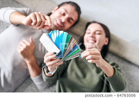 Hands of young woman lying on the floor next to her husband and holding palette 64763006