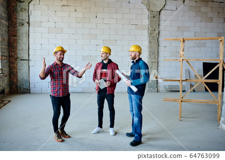Happy young engineer or builder explaining colleagues what else should be done 64763099