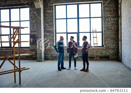 Young architects or contractors talking in the center of large unfinished room 64763111