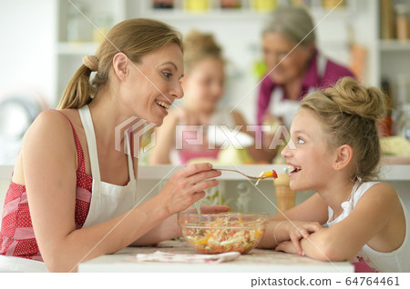 Portrait of cute little girl with her mother eating at kitchen table Portrait of cute little girl with her mother eating at kitchen table 64764461