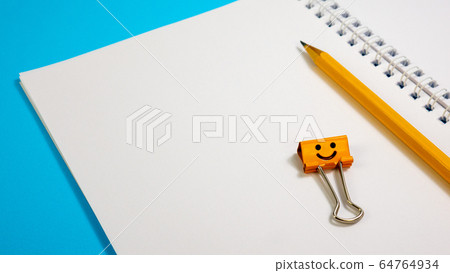 Blank Paper Notepad with Orange Color Pencils and Smile Binder Clip on Blue Background Blank Paper Notepad with Orange Color Pencils and Smile Binder Clip on Blue Background 64764934
