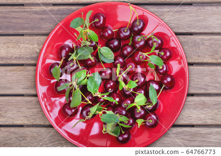 Red plate of ripe cherries with green leaves on a Red plate of ripe cherries with green leaves on a 64766773