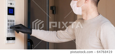 Man in face mask and gloves dials the code on the intercom and going in porch of his apartment. Pandemic covid-19 concept 64768419