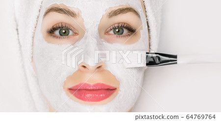 Facial beauty treatment. Closeup of pretty woman getting mask at spa salon. Cropped image of special brush in hands of cosmetologist applying white mud facial mask with on female face Facial beauty treatment. Closeup of pretty woman getting mask at spa salon. Cropped image of special brush in hands of cosmetologist applying white mud facial mask with on female face 64769764