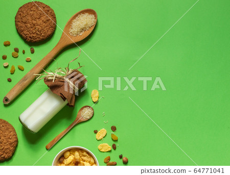 flatlay with a bottle of rice milk, corn flakes and dried fruit on a bright green background with space, horizontally flatlay with a bottle of rice milk, corn flakes and dried fruit on a bright green background with space, horizontally 64771041