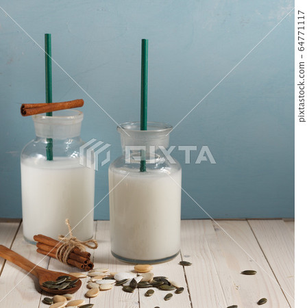 two serving bottles of vegetable milk made from pumpkin seeds on a blue background with cinnamon sticks 64771117