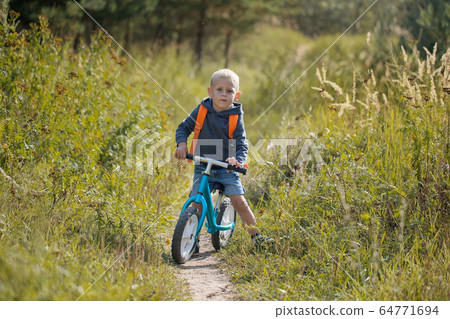 Toddler riding a balance bike along the path in Toddler riding a balance bike along the path in 64771694