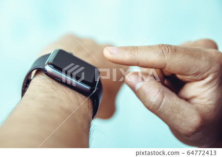 The man controls by touching his finger a smart watch on his hand The man controls by touching his finger a smart watch on his hand 64772413