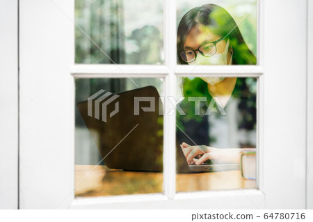 Young Asian woman wearing N95 mask and eyeglasses working on her computer at home Young Asian woman wearing N95 mask and eyeglasses working on her computer at home 64780716