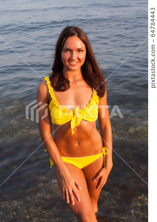Beautiful woman with long hair in yellow swimsuit sunbathes on a sea beach 64784443