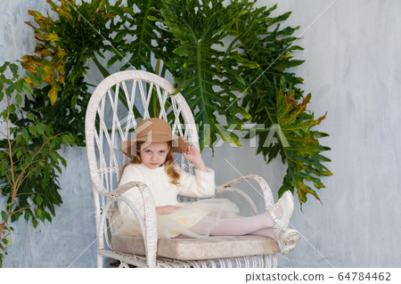 beautiful fashionable girl in a hat with fields sitting in a white chair 64784462