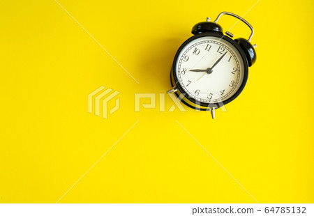 black alarm clock from 7 a.m. to 8 a.m. with bright yellow background and shadows from the changing light of the sun's movements in morning and working hours concept front shot black alarm clock from 7 a.m. to 8 a.m. with bright yellow background and shadows from the changing light of the sun's movements in morning and working hours concept front shot 64785132